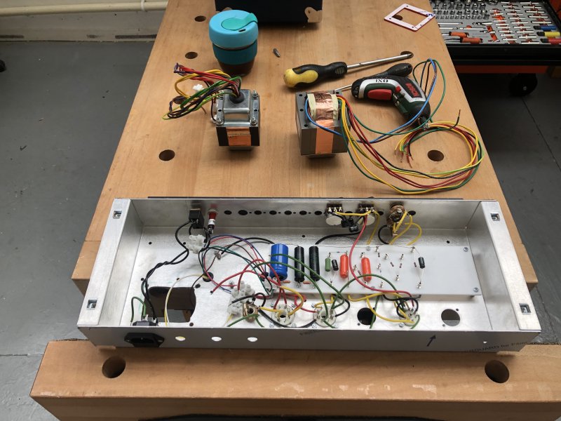 The chassis of the amp on the bench with the insides showing, revealing the point-to-point board and a hole where the old transformer was. Beside the chassis is the old and new transformer.