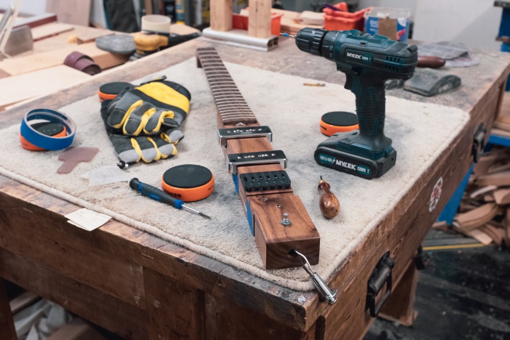 The wooden core of älgen on a workbench, with bits hanging off it, and a power-drill, gloves, screwdrivers and so forth sat next to it.