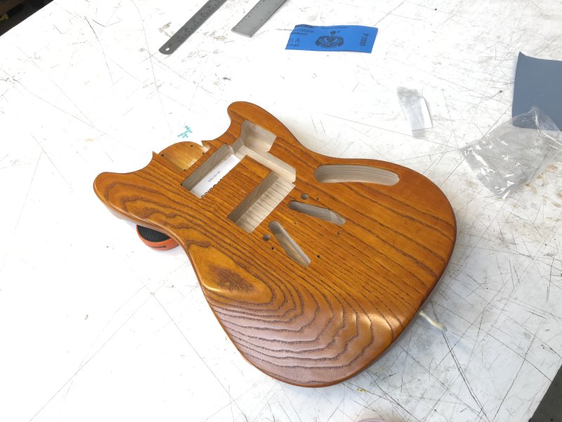 A mustang-style guitar body made in ash that is decidedly orange despite being stained with yellow wood stain.