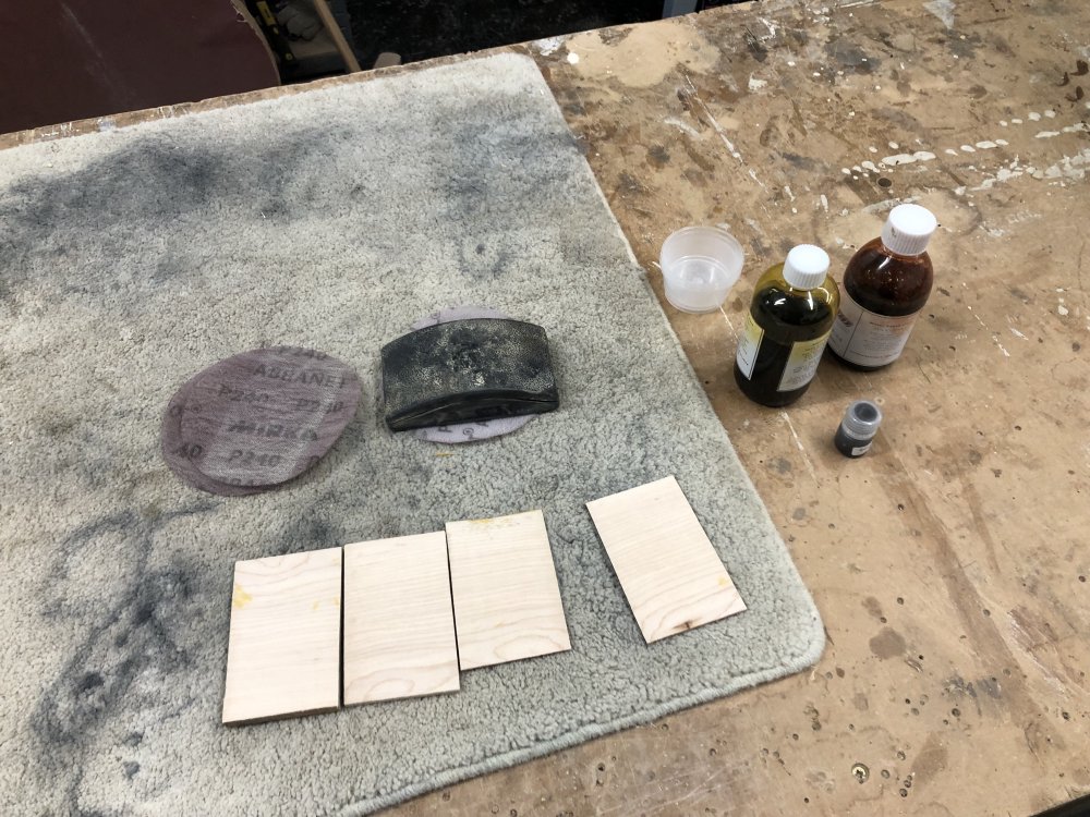 The four bits of wood on the workbench, this time not showing any stain as we're now looking at the backs of them. Beside this sit some pots of wood stain and some sanding disks.