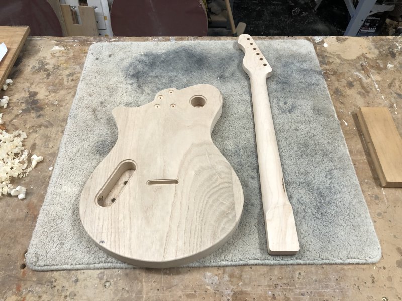 The body and neck sit beside each other on the workbench, with the new holes evident on the body, but no matching holes on the neck yet.