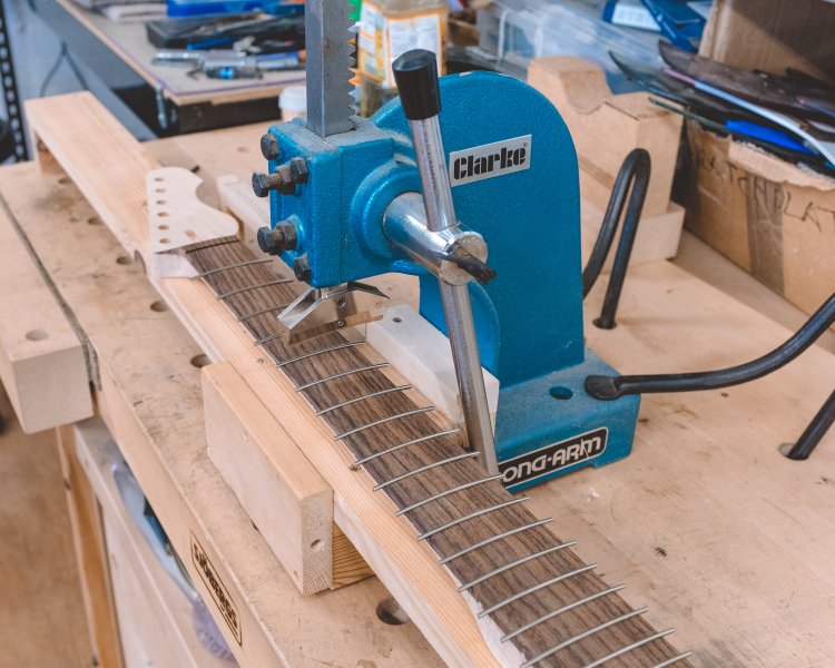 The neck sits under an arbour-press, now all the fret slots are filled with fret-wire, which hangs over each side as it hasn't yet been trimmed.