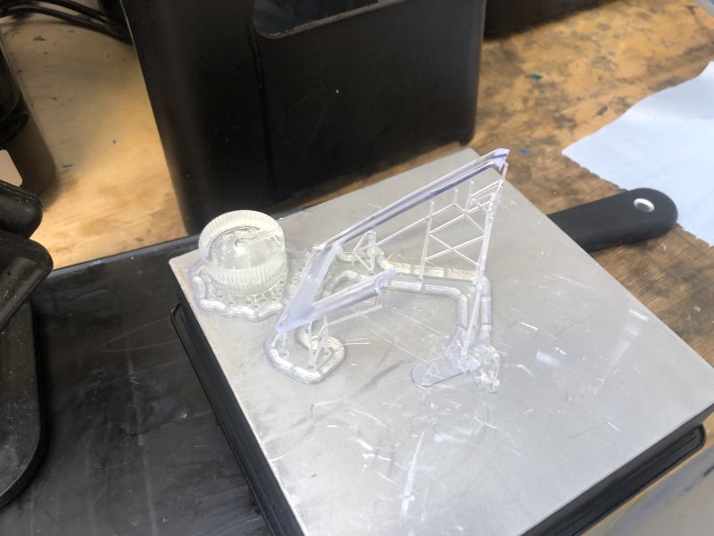 The build plate from a Formlabs printer taken out of the printer with a volume control and half a pickup ring printed on it, but half missing.