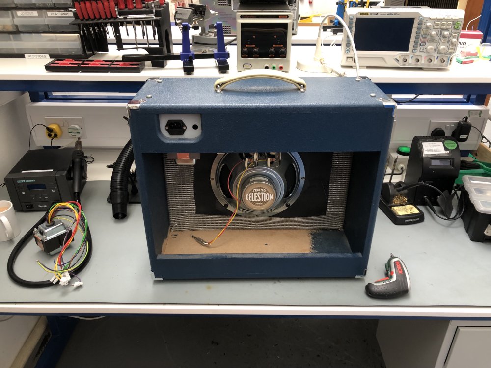 The rear view of an all-in-one amp cabinet sat on a workbench. The back is open, so you can see the speaker cone, which is unplugged, and the power socket on the chassis.