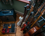 A rack of guitars sits next to an amp and pedalboard. The most obvious guitar on the rack is Älgen, which is part 3D-printed, making it stand out from all the other guitars.