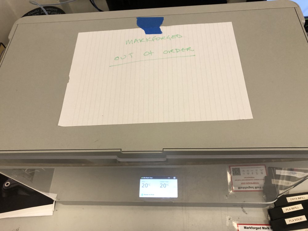 A boxy 3D-printer with a hand-written notice saying 'Markforged out of order' stuck to it.