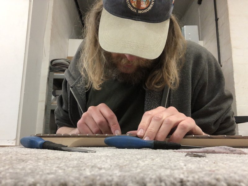 A picture of me taken from the workbench, looking down intently at the neck, as I hold it steady with one hand and work with a file in the other.
