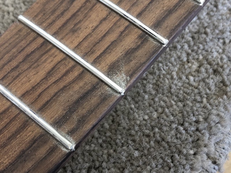 A close up of the fret-ends being worked on, with visible metal dust over the fretboard from where it has been worked.