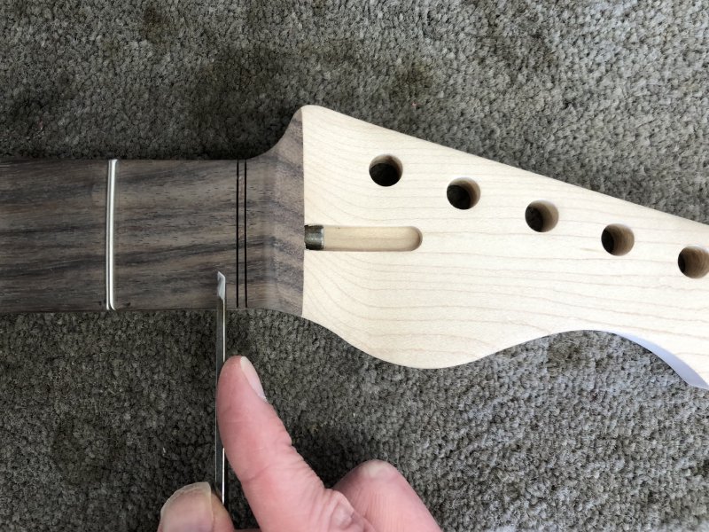 A close up of the top end of the neck in question, where you can see two saw-blade width slots have been cut where the nut would normally sit, but there's still wood to be removed to allow the nut to sit there. I'm holding a small chisel that I'm about to use to remove that wood.
