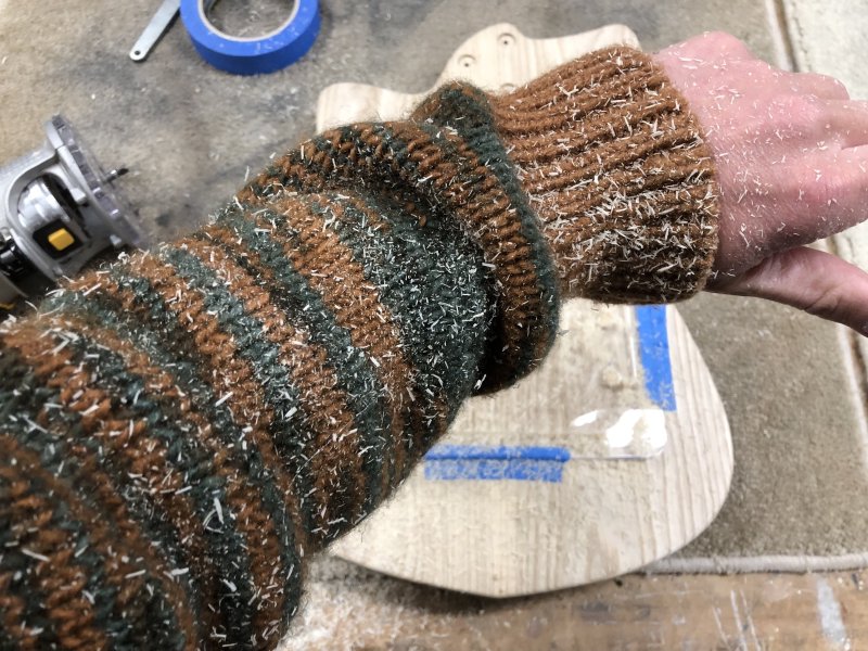 A picture of the orange and green sleeve of my sweater and my hand, all covered in fresh sawdust.