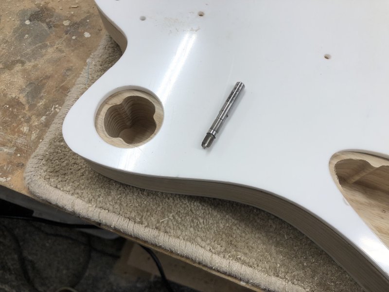 A small router bit sits on top of a white acrylic template that sits on top of the guitar body.