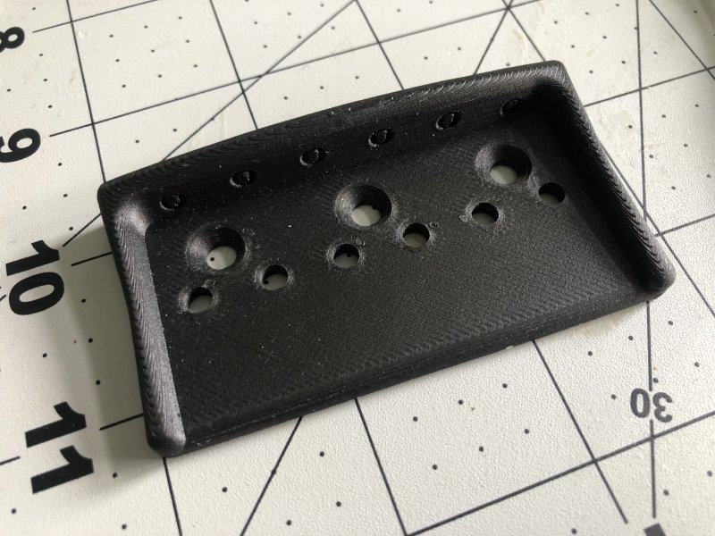 A black plastic looking guitar bridge plate sits on a craft board.