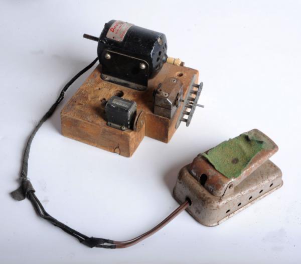 A wooden block has a motor on it, connected by a cable to a foot pedal that probably lets you control the speed of the motor. On the motor spindle is an unwound pickup.