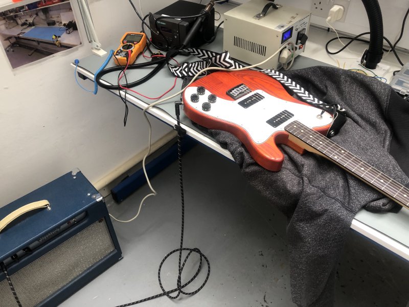 The same workbench, but now there's an orange guitar sat on it, sat upon a grey hoodie that I was wearing before as I didn't come prepared for guitar surgery.