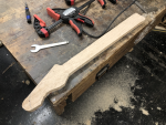 A work-in-progress guitar neck sits on the workbench, surrounded by sawdust on the floor.