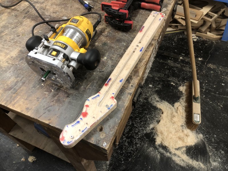 The neck with template sits on the workbench, and now the wood perfectly follows the template outline. On the floor is a large pile of swept up wood dust that was made in the process.