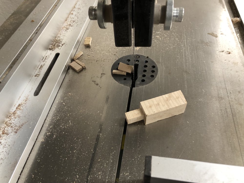 A close up of the peg-like bit of wood I've made sat on the table of the band-saw, with some small off-cuts behind.