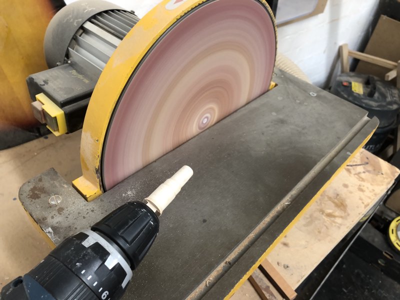 My peg is clamped into the chuck of a power-drill hand-tool, and behind that you can see a spinning disk sander.