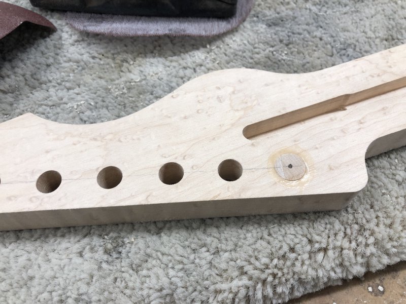 A close up of the front of the headstock, showing the same five holes plus the plug, but the plug here is still slightly proud of the front and you can see the wood glue overspill. In the middle of the plug is an indent from the bradawl ready to guide the drill bit when I re-drill the hole.