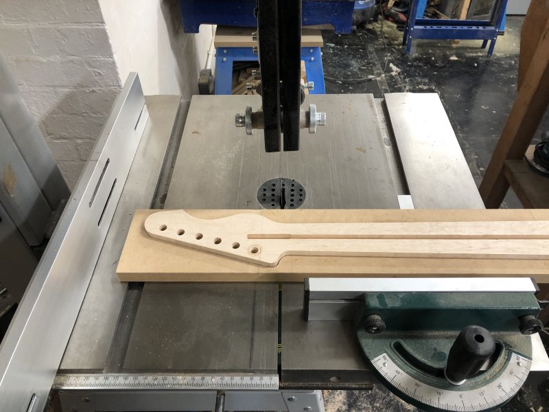 The neck sits in a jig that gives me an edge parallel to the centreline of the neck, and makes it easier to push up against the fences on the band-saw. All of this sits on the band-saw table ready for cutting.