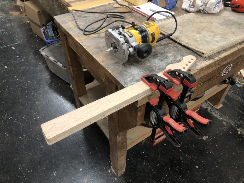 The neck is clamped to a workbench, with most of the neck hanging off the edge so that when I trim the fretboard flush it I don't also cut the bench. Beside the neck on the workbench is a plunge-router with guide bit in place.