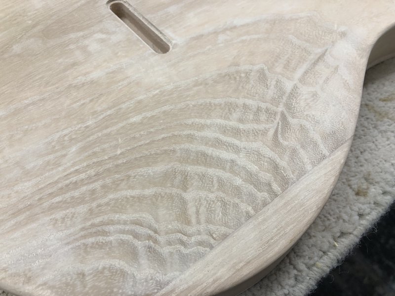 A close up on the back of the guitar body, and you can see where the grain of the wood runs in bands, those bands are now much lighter than the wood itself, due to the filler sitting inside the grain.