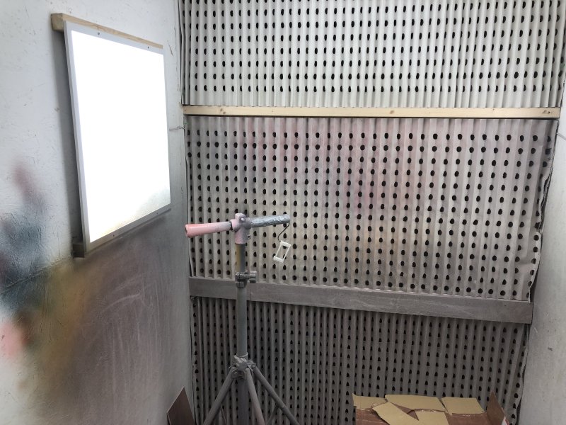 The inside of a spray-booth, in which there is a stand that usually holds guitars for spraying, and instead is holding a small spindly 3D-print that would fit in the palm of your hand.