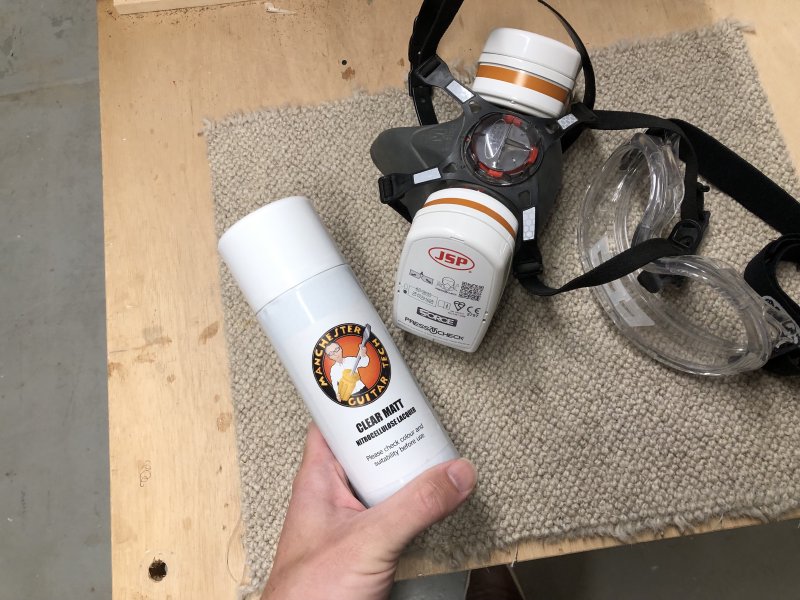My spray booth PPE of respirator and goggles sit next to my hand holding a can of spray on lacquer.