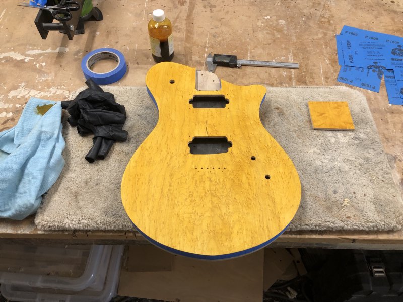 The guitar body sits on the workbench, still with masking tape around teh sides, but now the face is a bright yellow colour.