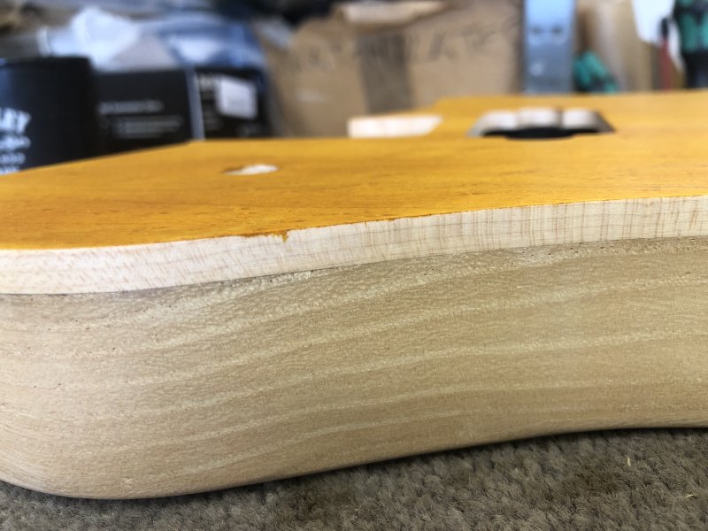 A close up of one section of the side of the guitar body, where you can see a bit of the yellow stain has seeped between the masking tape and the body. It's only a millimetre or two, but given how vivid the stain is, it's quite noticable.