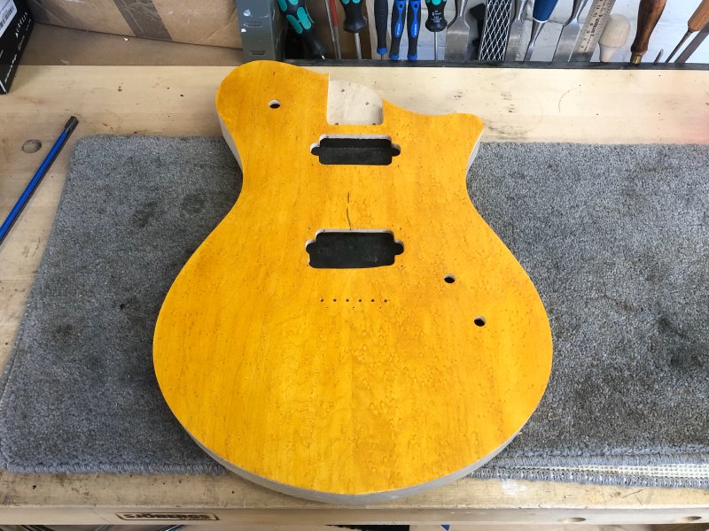 The guitar body sits on a different workbench in the same pose. The tape is gone, but there is a deeper yellow colour to the face now.
