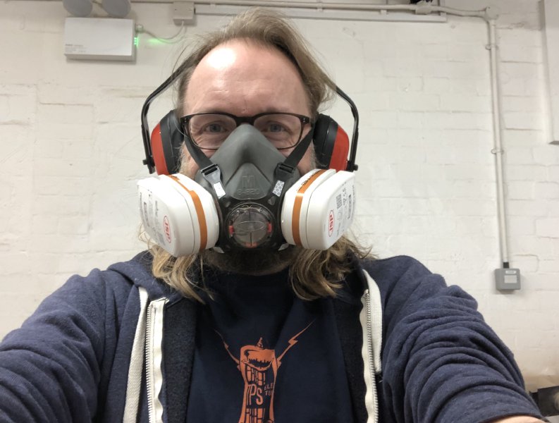 A selfie of me wearing a respirator and ear-defenders and trying to smile.