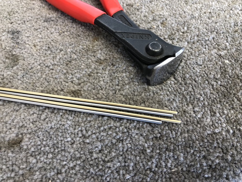 A view of 4 narrow (2mm) metal rods sat on a workbench next to some metal snips. Two of the rods are silvery in colour, and two are brass.
