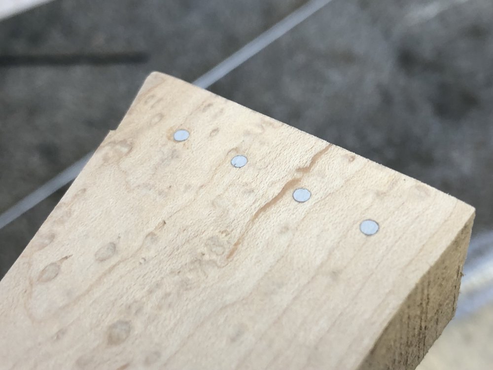 A close up of the same four bits of dowel mounted in wood as in the previous picture, but now they have been worked to be smooth and flush with the wood, leaving small shiny metal circles in the wood.