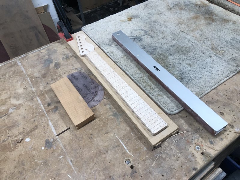 The neck sits on the workbench, with a long sanding bar on one side, and a radiused sanding block to the other.