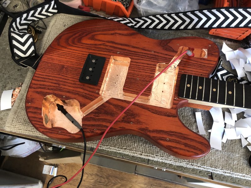 A yet later view of the same guitar body, only now all the cavities have shiny new tape in them, and there is a set of multimeter probes touching the furthest apart points on the new shielding.