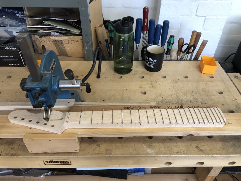 The neck sits on a workbench with all the frets in, with overhang visible on all the frets on both sides.