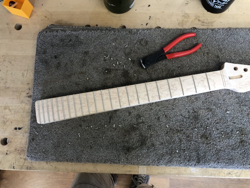 The neck now sits with all its frets flush with the side of the neck, and a lot of bits of metal fret clippings to either side of it.