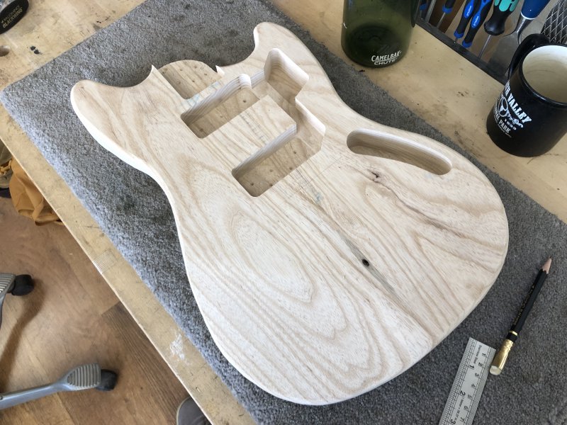 The raw body of this guitar sits on the workbench, and you can see a pencil line to indicate where the bridge should go.