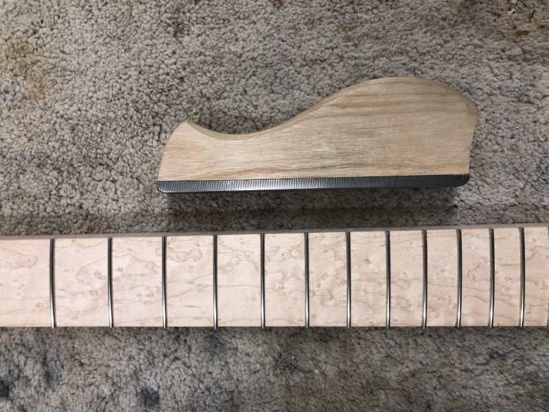 A top down view of the fretboard of a guitar neck with frets put in it, and next to it is a rasp used to level the fret ends.