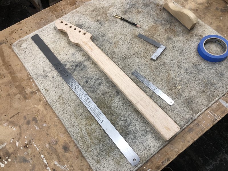 The neck sits face down on the workbench with a bunch of rulers, a pencil and a set square next to it. On the back of the neck you can see lines to indicate where to carve the back.