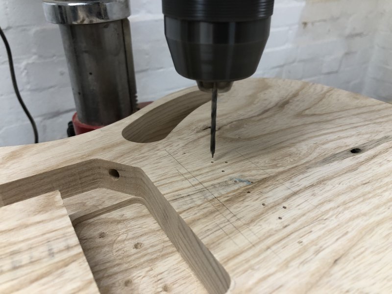 A spinning 3mm brad-point drill bit is about to enter one of the pilot holes I drilled earlier for where the strings go through this guitar body.
