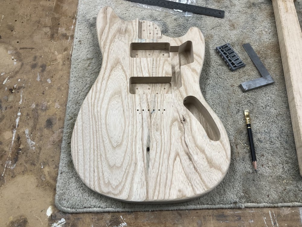 The guitar body is sat on the workbench, and you can see six well defined holes for the strings to pass through where the bridge will sit, and 3 pilot holes for the bridge mounting screws.