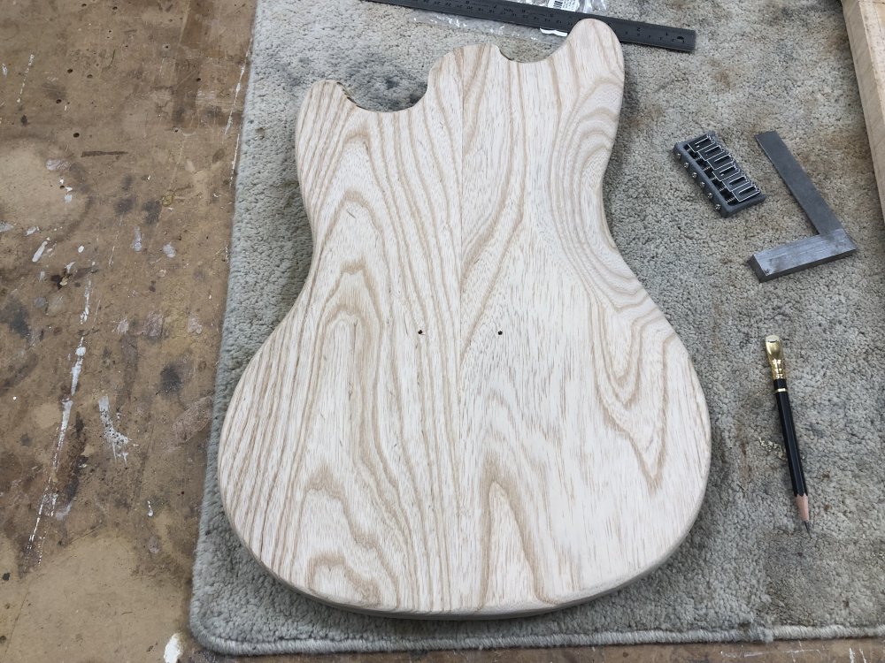 The guitar body is flipped over to show the back, and where the six holes were on the front you can just see the outer two have made it all the way through.