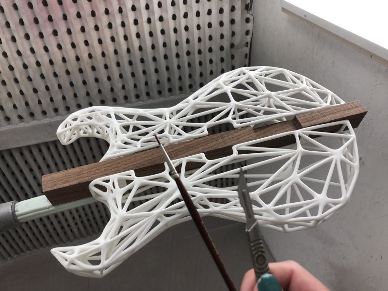 A view of the 3D-print suspended in the spray booth, and in my hands are a scalpel and a paint brush.