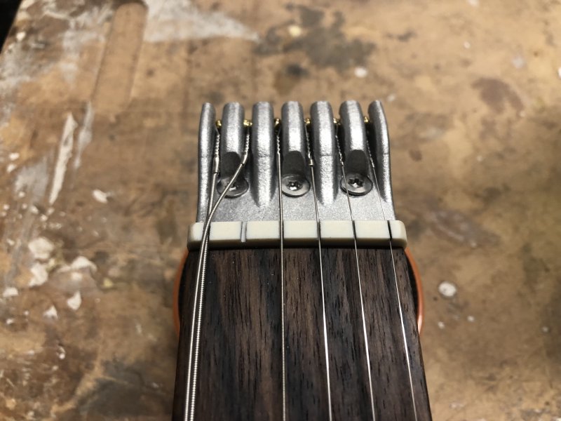 A close up on the nut of the guitar, showing the view as I cut the nut-slots. All the strings are in place except one, which has been slackened and pulled to one side, resting in the slot of a neighbouring string, to allow me to cut that one slot.
