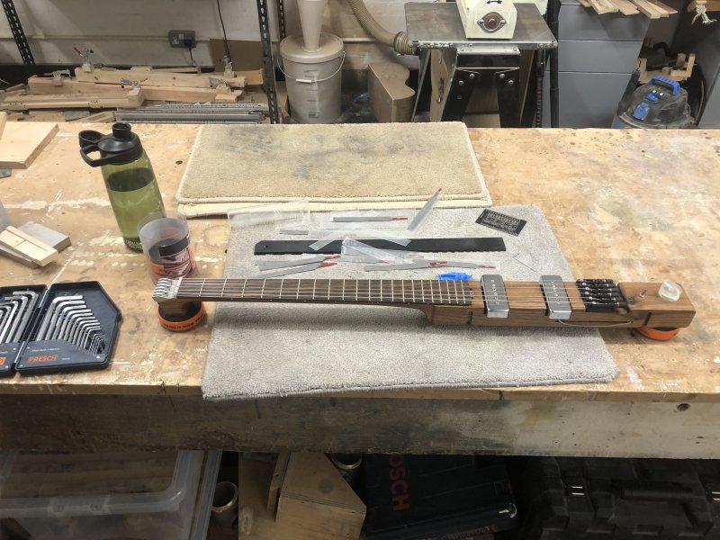 The core body of Älgen, which is the neck and the centre of the body area as a single piece of wood, sits on the workbench, strung up and surrounded by tools ready for set-up: nut-slot files, a notched ruler, and a small card for measuring string heights.