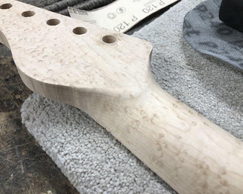 A close up of an in-progress neck carve, showing the transition between the headstock and the back of the neck. The neck is made from bird's eye maple.