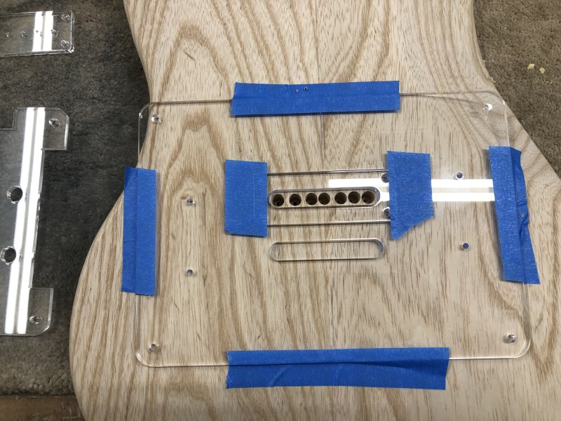 A top down view of the back of the guitar body, still with template attached, shows a row of 7 neat holes drilled into the body in the gap in the template.