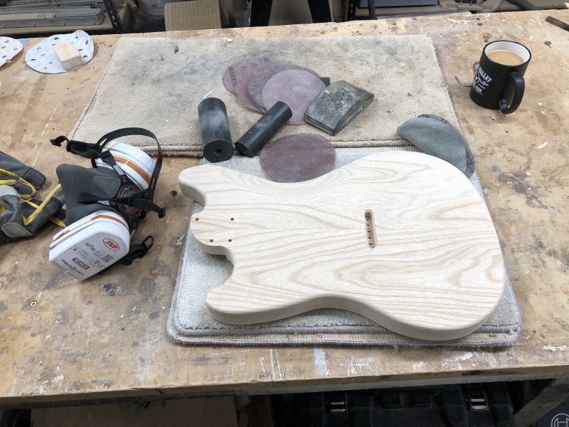 The guitar body sits on the workbench upon a carpet mat again, and is now surrounded by sanding disks and my respirator PPE.